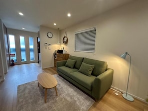 A living room with a green sofa, a round wooden table, and a floor lamp. - AND HOME (Osaka)