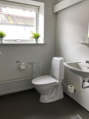 Un baño moderno con inodoro, lavamanos y ventana con dos plantas en macetas.