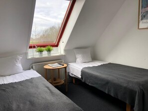 Un alojamiento pequeño de una sola habitación con techo inclinado, dos camas, una mesita y un ventanal con vistas a árboles.