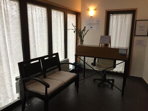 Un área de recepción con un mostrador, dos sillas y una planta en maceta.
