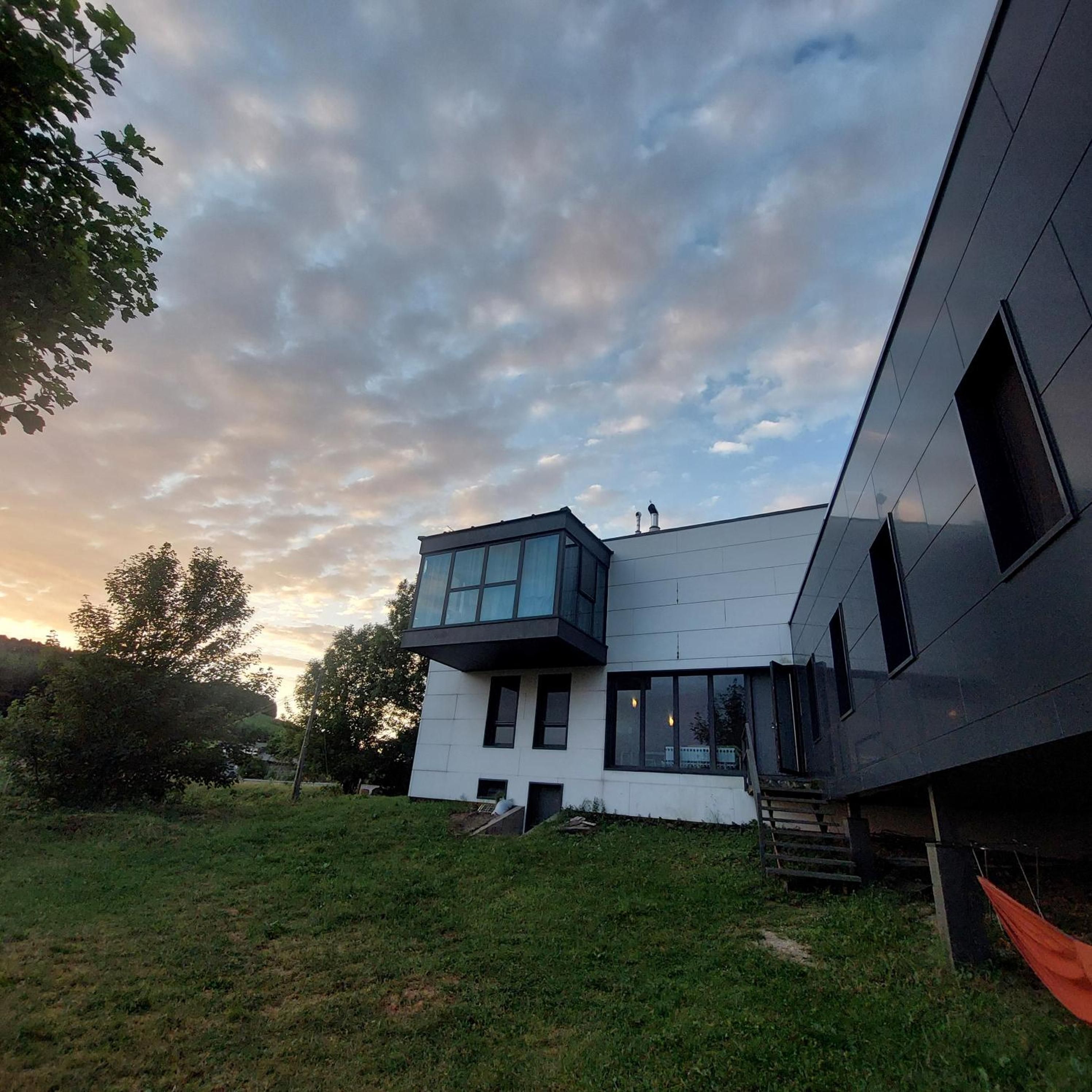 A modern two-story house with a flat roof, large windows, and a visible chimney.