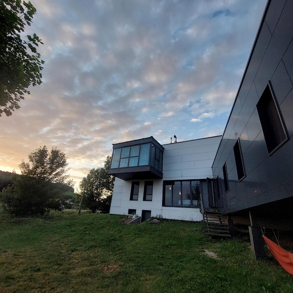 A modern two-story house with a flat roof, large windows, and a visible chimney.