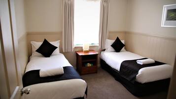A hotel room with two single beds, a small wooden nightstand, a window with curtains, and a framed picture on the wall.