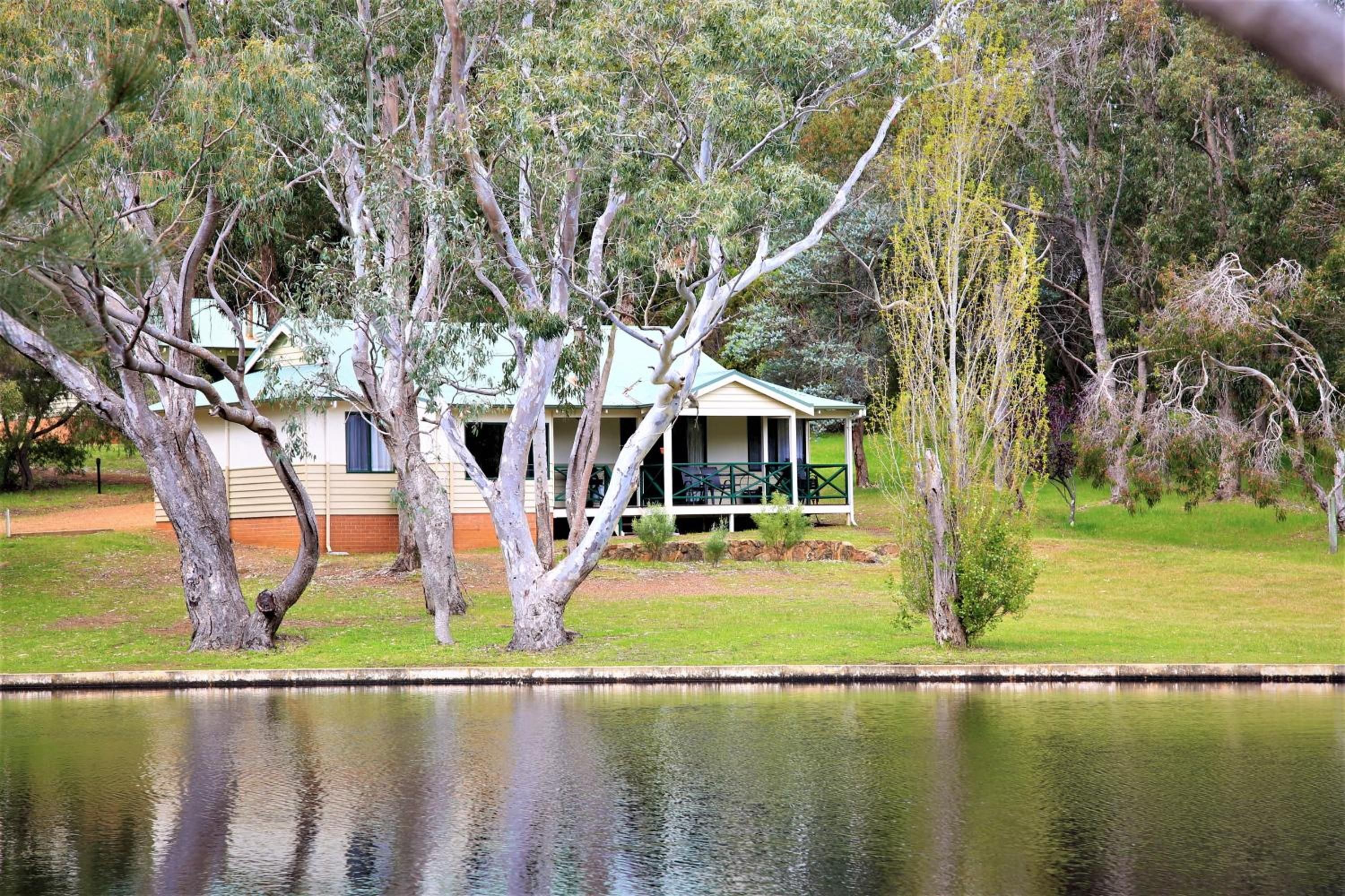A house with a porch, surrounded by trees and a body of water.