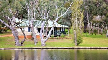 A house with a porch, surrounded by trees and a body of water.