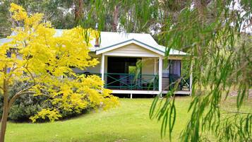 A single-story building with a porch, surrounded by lush greenery and a tree with yellow leaves.