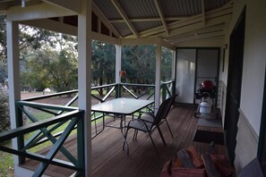 A covered outdoor area with a table and chairs, a grill, and a view of trees.