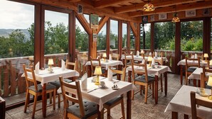 Un restaurant amb diverses taules i caires, grans finestres que ofereixen vistes cap a l'exterior i una estructura de sostre de fusta.