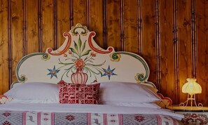 Una cama con un cabecero decorativo, un cojín estampado y una lámpara de noche.