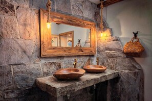 Un baño rústico con pared de piedra, espejo con marco de madera y lavabo de madera.