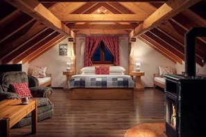 Quarto de sótão aconchegante com cama grande, vigas de madeira, lareira e decoração rústica.