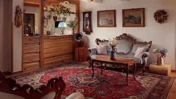 Un salon traditionnel avec un canapé en bois, un tapis à motifs et une radio d’époque.