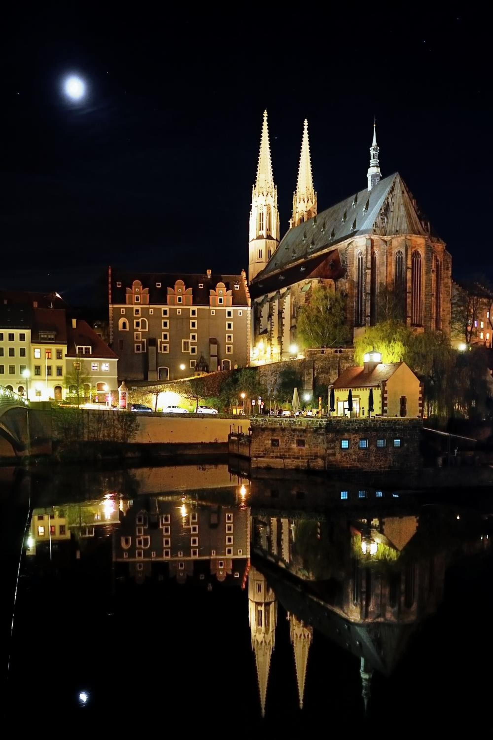 A historic church with twin spires and a large central tower, reflecting in a calm body of water.