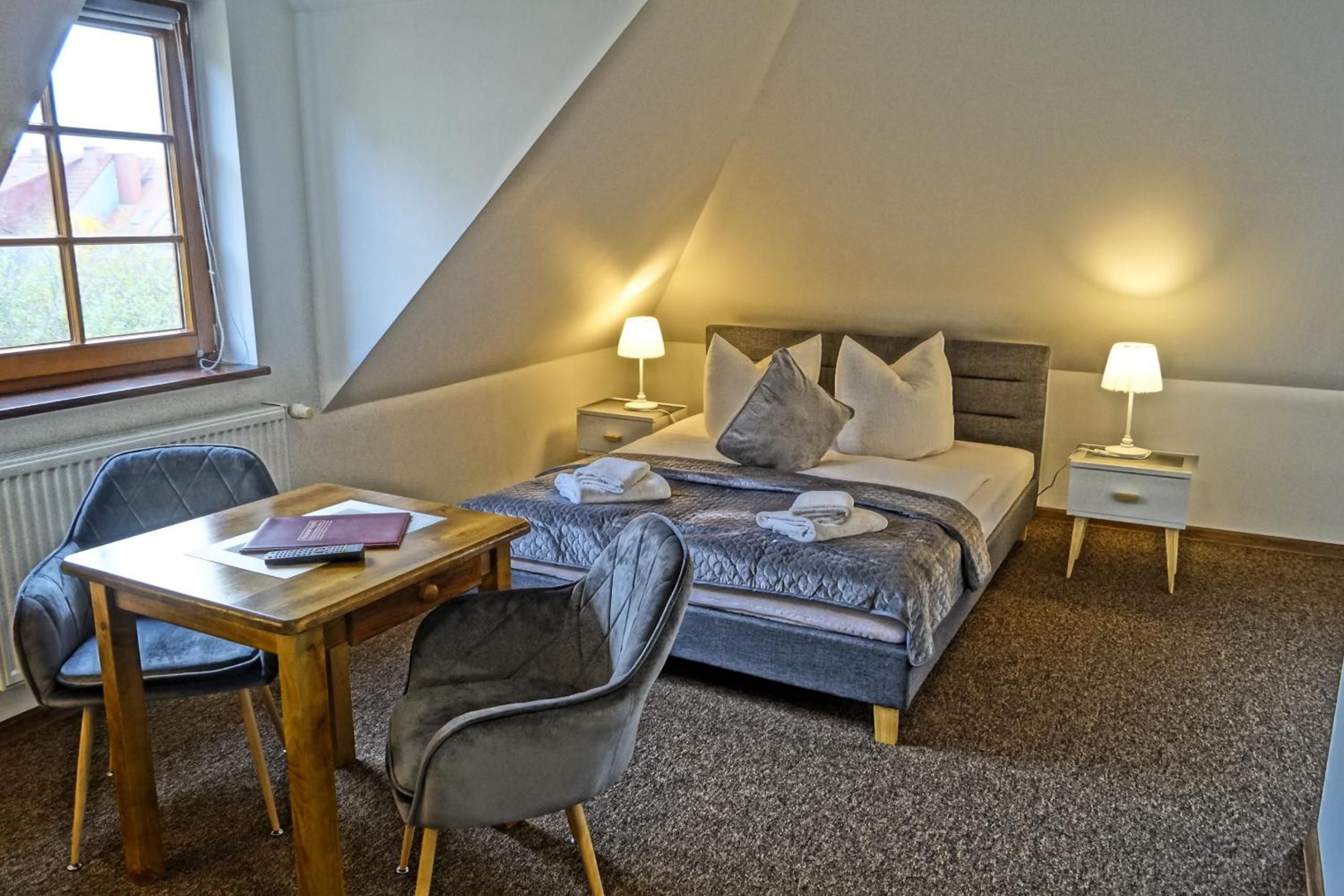 A bedroom with a bed, two bedside tables, a desk, and two chairs.
