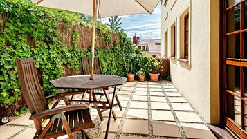 An outdoor patio with a table and chairs, surrounded by potted plants and a wooden fence.