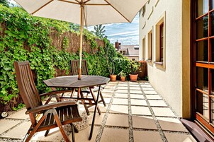 Un patio al aire libre con una mesa y sillas, rodeado de plantas en macetas y una valla de madera.