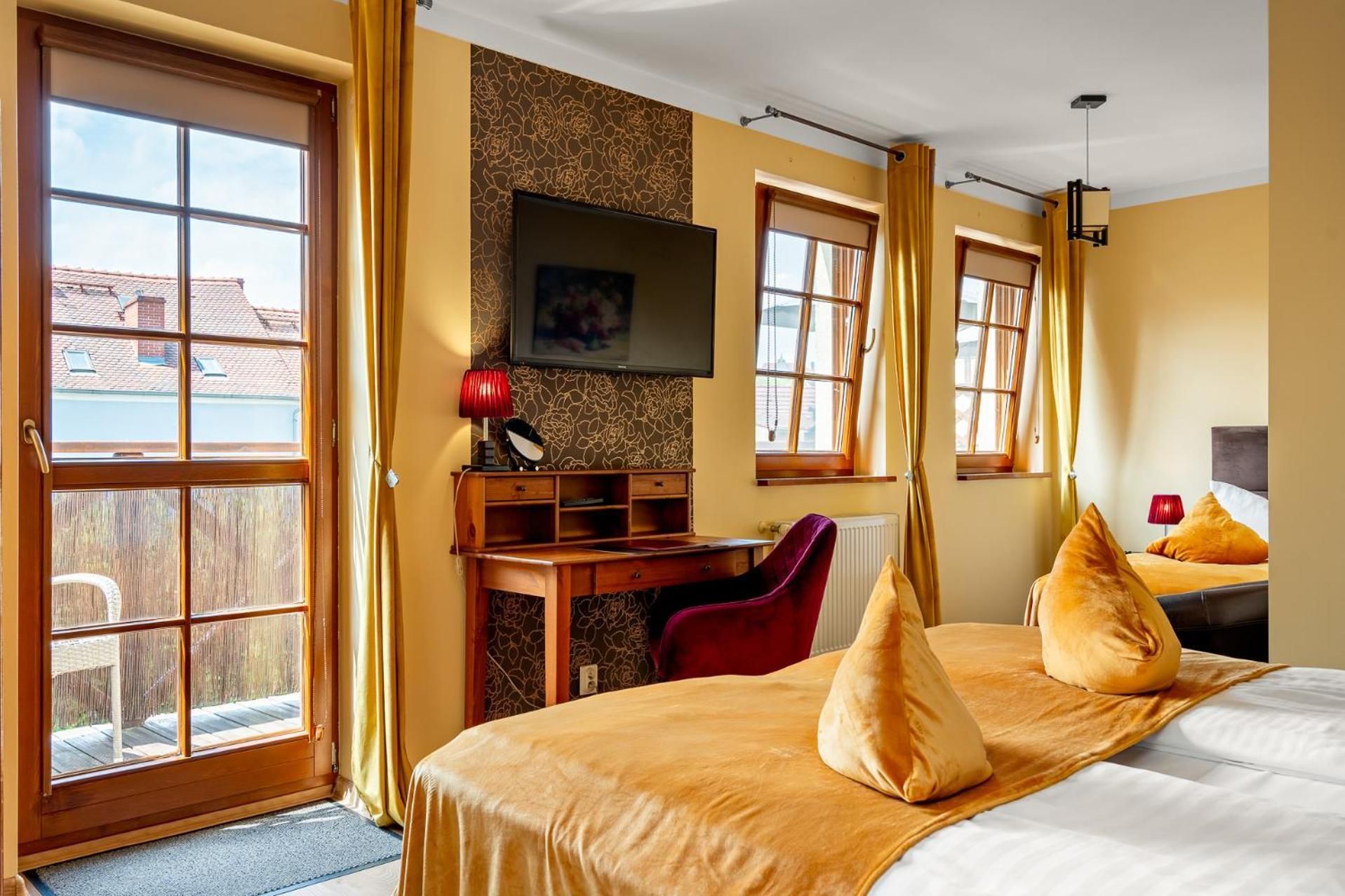 A hotel room with a bed, a desk, a television, and large windows.