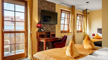 A hotel room with a bed, a desk, a television, and large windows.