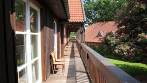 A wooden deck with a railing, a chair, and a view of a building with a red-tiled roof. - Büchtmannshof (Wietze)