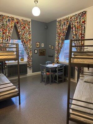 A dormitory room with bunk beds, a table with chairs, and curtains with a floral pattern. - Stf Landskrona Hostel (Landskrona)