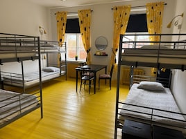 Ett studentrum med våningssängar, ett bord, stolar och ett element.