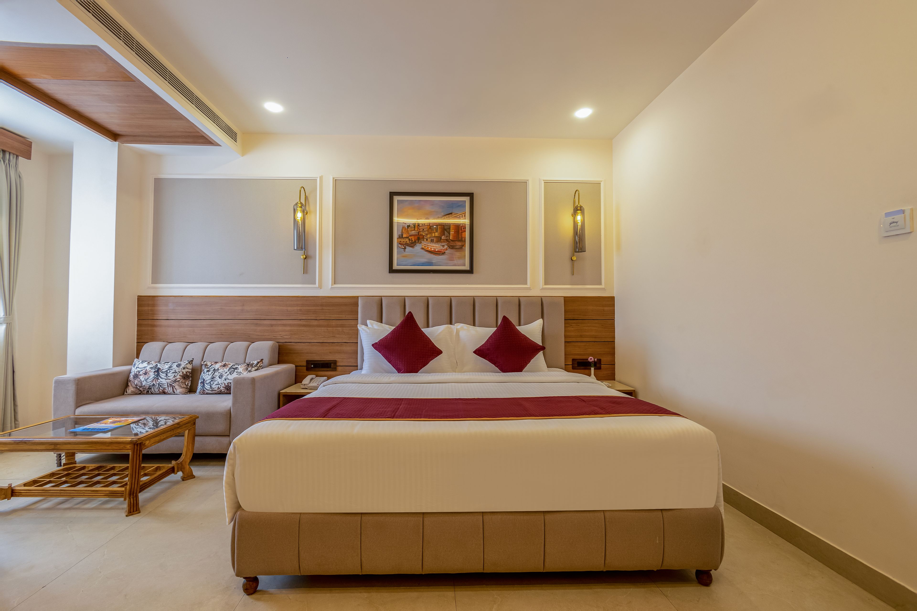 A hotel room with a large bed, a sofa, a coffee table, and a painting on the wall.