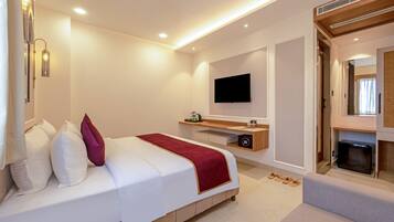 A modern hotel room with a large bed, a flat-screen TV mounted on the wall, a small wooden side table, and a built-in safe.