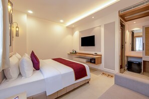 A modern hotel room with a large bed, a flat-screen TV mounted on the wall, a small wooden side table, and a built-in safe. - Sterling Varanasi (Varanasi)