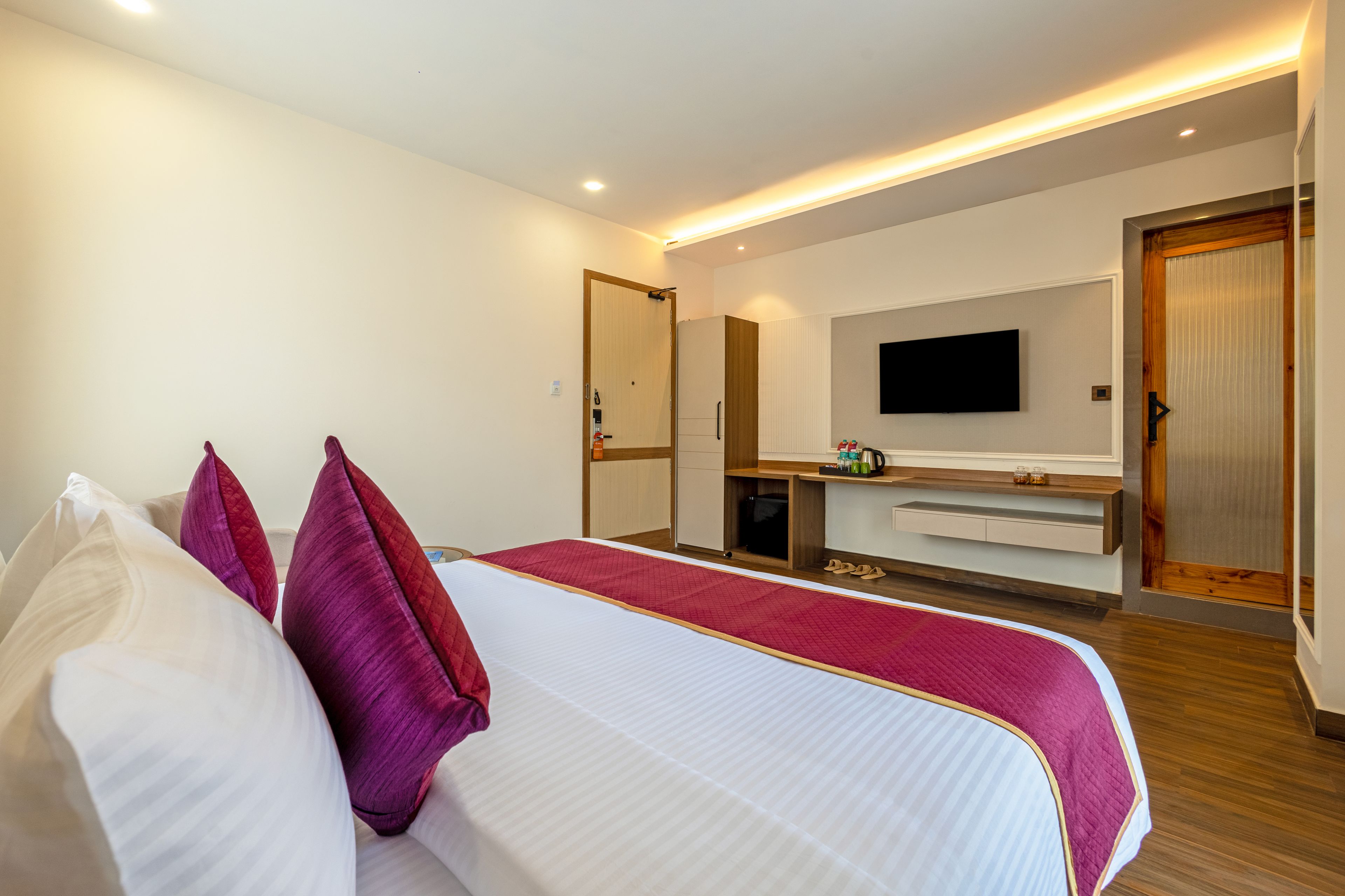 Una camera d'albergo con un letto, una televisione, un minibar e una porta in legno.