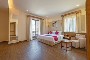 Habitación de hotel con una cama grande, un área de descanso con una silla, una mesita y un balcón con vistas.