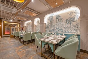 Interior de restaurante con mesas dispuestas para comer, una pared decorativa con ilustraciones de plantas e iluminación empotrada en el techo.