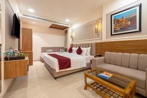A hotel room with a bed, a sofa, a coffee table, a TV, and a painting on the wall.