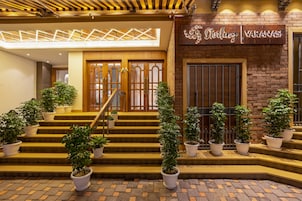A hotel entrance with a staircase, potted plants, and a sign reading 'Sterling Varanasi'.
