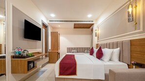 Quarto de hotel moderno com uma cama grande, televisão de tela plana, guarda-roupa de madeira, mesa de cabeceira e um pequeno espaço de estar.