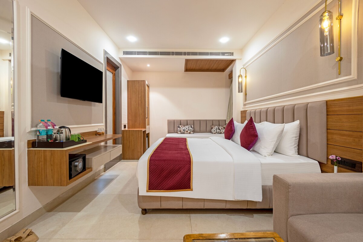 Una habitación de hotel moderna con una cama grande, un televisor de pantalla plana, un armario de madera, una mesita de noche y una pequeña zona de estar.