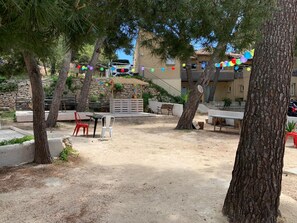 Eine Terrasse im Freien mit Tischen und Stühlen, umgeben von Bäumen und einer Steinmauer.