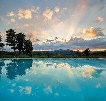 A clear swimming pool reflecting the sky and trees, surrounded by a natural landscape.