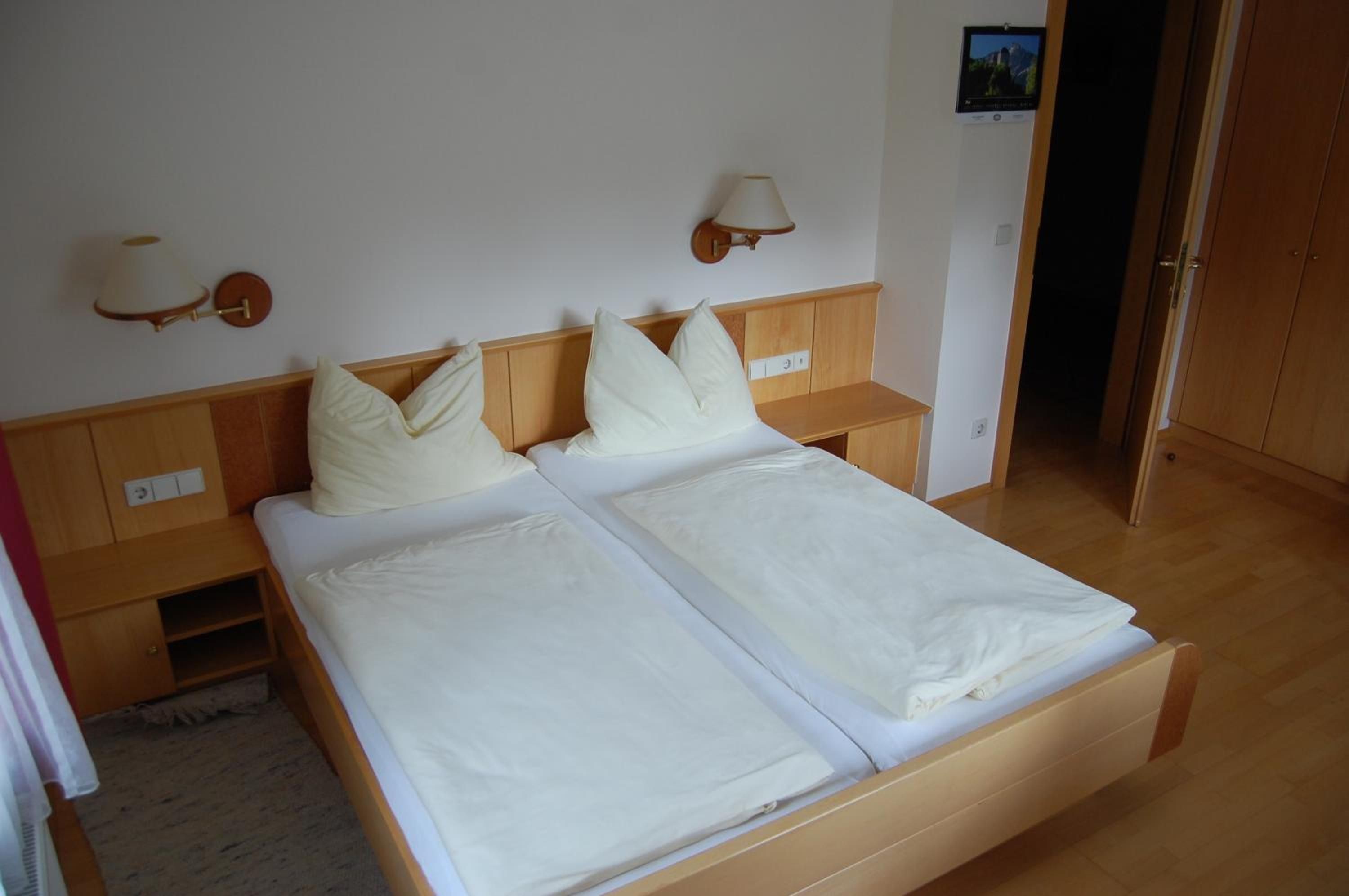 Ein Doppelbett mit zwei Kissen, ein Nachttisch, eine Lampe und ein an der Wand befestigtes Fernsehgerät.