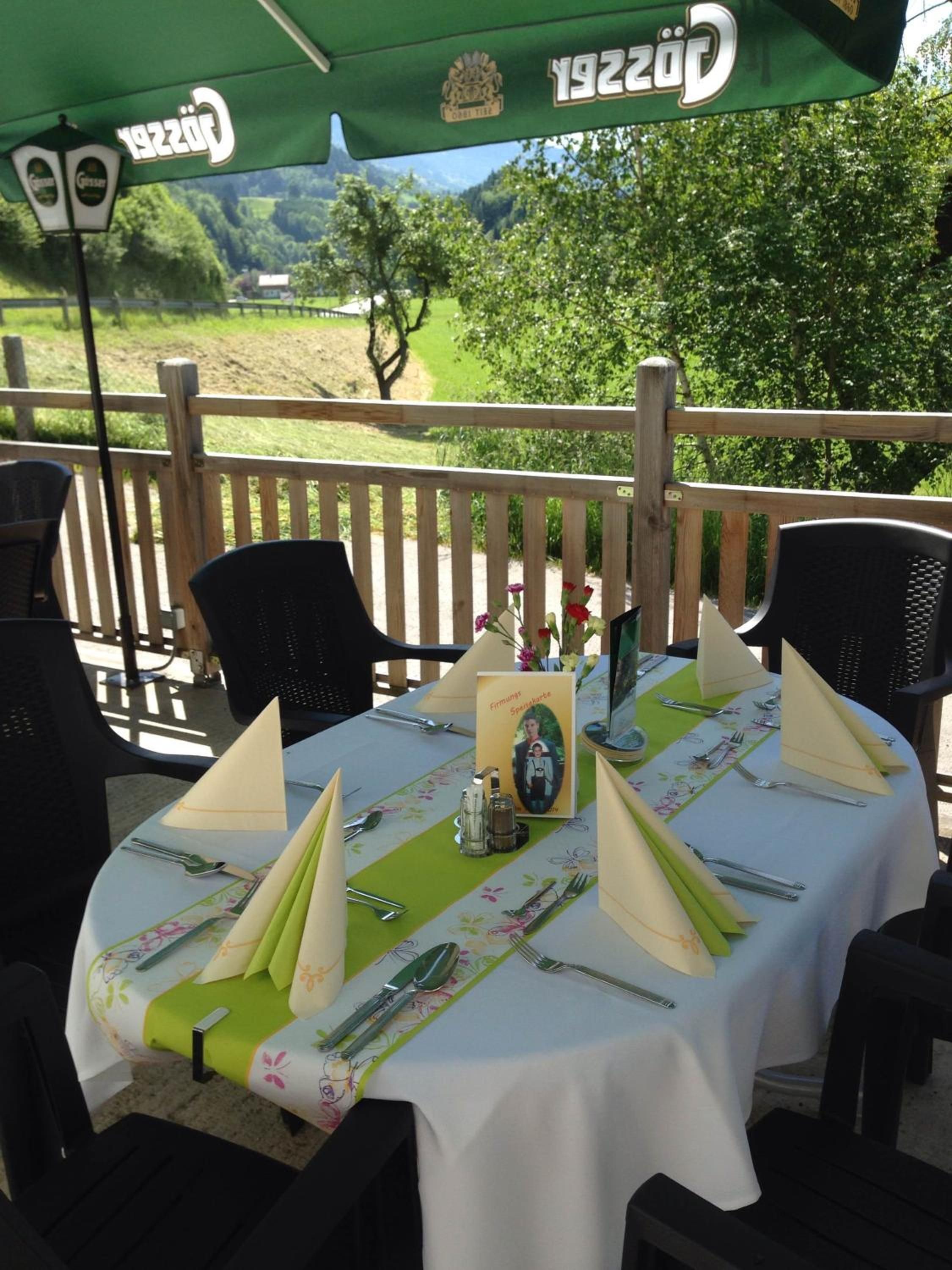 Ein Essbereich im Freien mit einem Tisch für zwei Personen, einem grünen Sonnenschirm und einem schönen Ausblick im Hintergrund.
