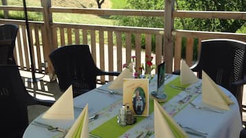 Un área de comedor al aire libre con una mesa lista para dos personas, una sombrilla verde y una vista panorámica al fondo.