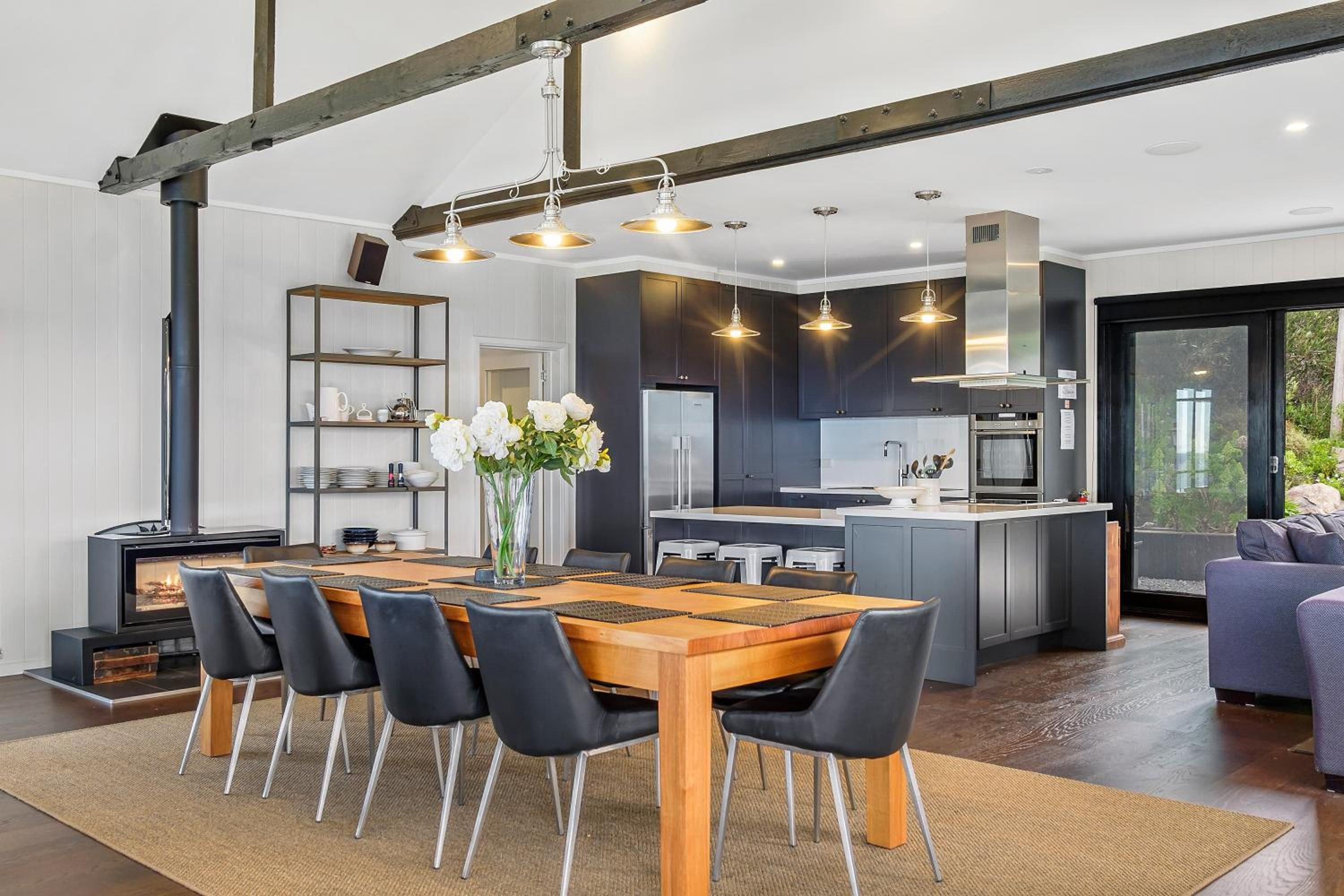 A modern kitchen with dark cabinetry, a central island, and a dining area with a wooden table and black chairs.