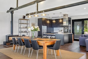 Cocina moderna con armarios oscuros, una isla central y un comedor con mesa de madera y sillas negras.