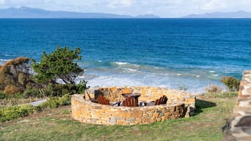 A stone fire pit with seating, overlooking a coastal view with the sea and mountains in the distance.