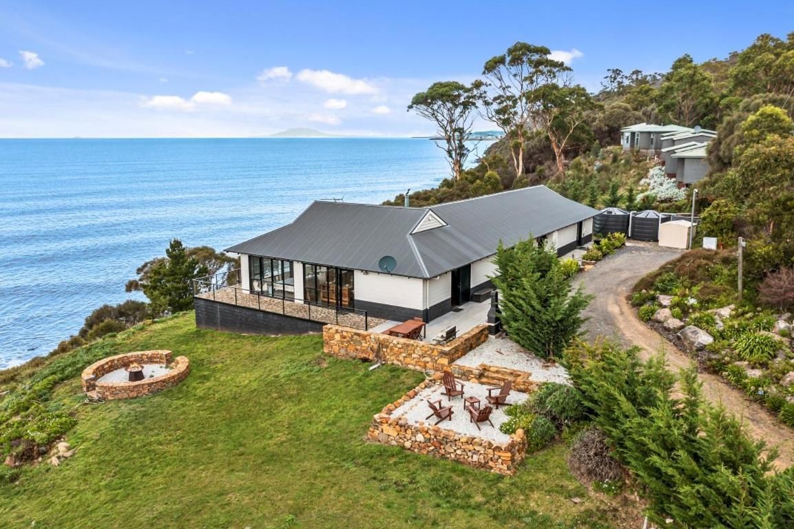 A modern house with a large glass window, a stone patio, and a view of the sea.