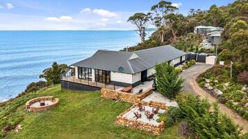 A modern house with a large glass window, a stone patio, and a view of the sea.