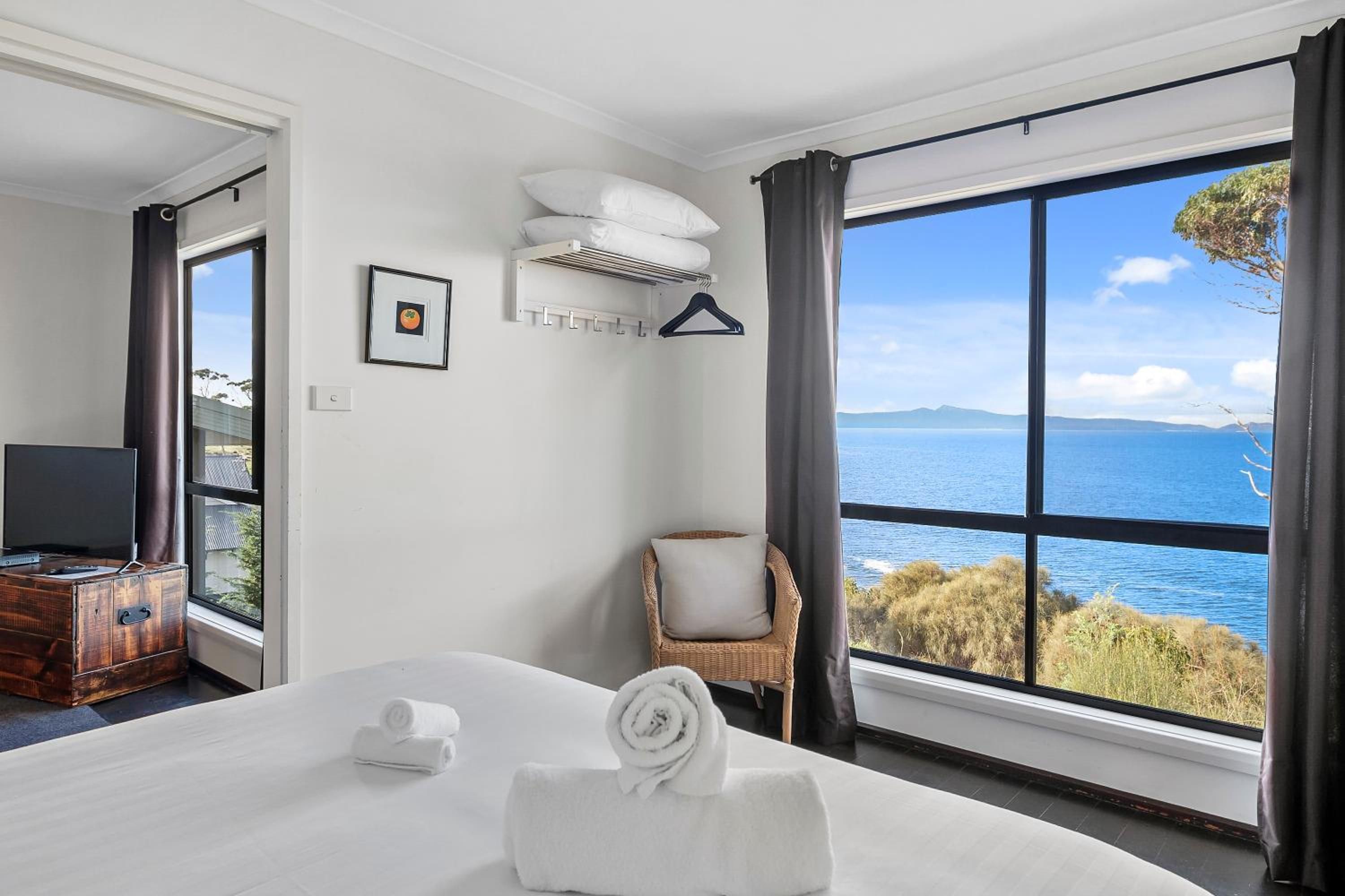 A hotel room with a large bed, a television, a chair, and a view of the sea.