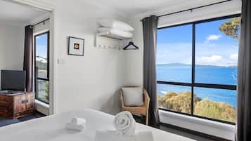 A hotel room with a large bed, a television, a chair, and a view of the sea.