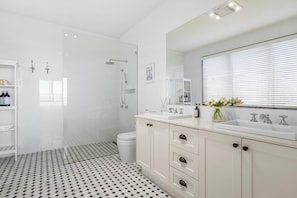 Un baño moderno con ducha, inodoro y tocador con un espejo grande.