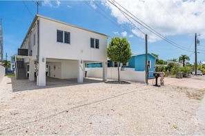 A two-story building with a covered parking area and a small tree in front. - The Waves. (Key Largo)