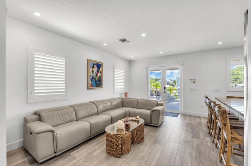A modern living room with a sectional sofa, a glass coffee table, and a dining area with wooden chairs.